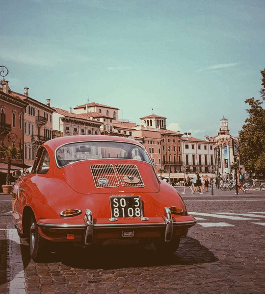 In a European, stone city, a man in a red car travels down the road.